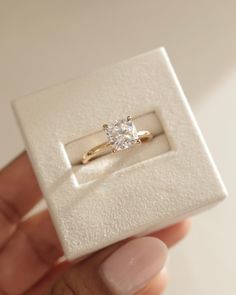 a hand holding a ring with a diamond in it's center and the inside of its box