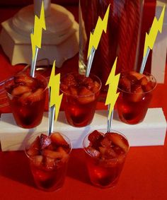 four glasses with strawberries in them are on a red tablecloth and have yellow lightning sticks sticking out of them