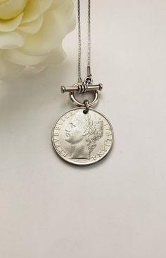 This vintage coin necklace will soon become a favorite go-to necklace. It features an Italian pre-euro silver-tone coin that dangles from an 18" stainless steel chain with a front toggle clasp. Your choice between a 50-lire (24mm or 7/8" in diameter) coin or a 100-lire (27mm or 1" in diameter) coin. Just a beautiful Italian heritage gift! Welcome to Recycled Finery!  I repurpose old jewelry, coins, beads, vintage buttons, watch parts, and charms into new jewelry.  My ever-growing collection of these materials comes from estate sales, rummage sales, antique and thrift stores, and family and friends' collections they no longer need or want. I have fun putting these new pieces together and hope you will find them fun to wear and as unique gifts for your loved ones.     Please note: Because my Classic Engraved Sterling Silver Coin Necklace, Classic Silver Necklace With Coin Pendant, White Gold Necklace With Coin Pendant, Sterling Silver Coin Medallion Necklace Nickel Free, Classic Medallion Necklace With Coin Pendant, Sterling Silver Coin Pendant Medallion Necklace, Vintage Charm Coin Necklace With Round Pendant As Gift, Vintage Charm Medallion Coin Necklace As Gift, Vintage Charm Medallion Coin Necklace For Gift