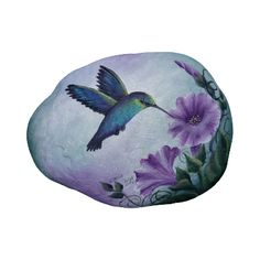 a painting of a hummingbird flying over purple flowers on a rock with green leaves