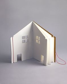 an open book with a house cut out on the inside and red string attached to it