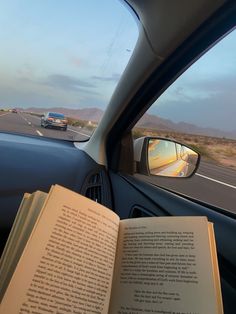 an open book sitting in the passenger seat of a car next to a road with cars on it