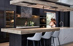 a modern kitchen with black cabinets and marble counter tops, bar stools and an island in the middle