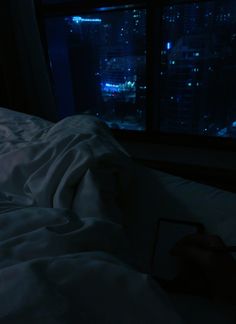 a person laying in bed at night with the city lights lit up from behind them