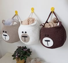 three crocheted baskets with faces hanging from hooks on the wall next to a potted plant