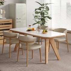 a dining room table with four chairs and a potted plant in the corner next to it