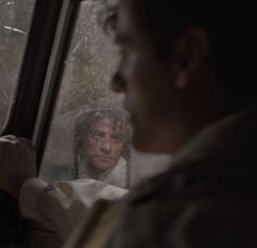 a man sitting in the passenger seat of a car looking out the window at another person