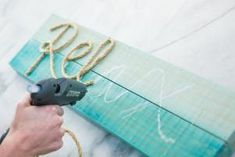 a person using a power drill to paint the letters on a wooden sign with rope