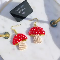 a pair of red and white beaded mushroom earrings sitting on top of a marble table