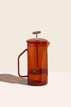 a red glass coffee pot with a handle and lid on a white surface, in front of a plain background