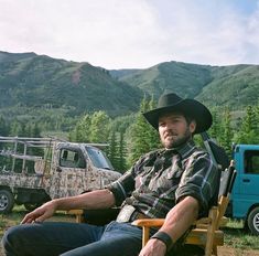 a man wearing a cowboy hat sitting in a lawn chair next to a camper