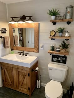 a white toilet sitting next to a bathroom sink under a wooden mirror mounted above it