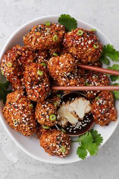 a white bowl filled with meatballs covered in sesame seeds and garnished with cilantro