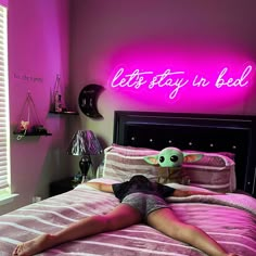 a woman laying on top of a bed next to a neon sign that says let's stay in bed