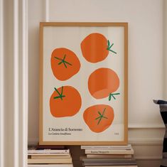 a framed poster with four oranges on it in front of a stack of books