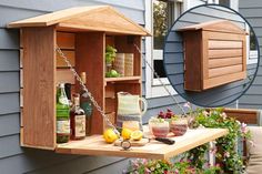 a wooden shelf with bottles and glasses on it next to a house that has flowers in the front yard