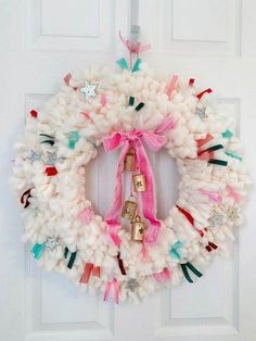 a white wreath with pink ribbon and bells hanging from it's side on a door