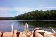 two women laying on the back of a boat with trees in the background and water behind them