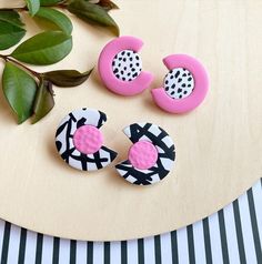 three pink, black and white buttons sitting on top of a wooden table next to green leaves