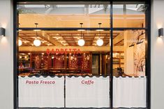 the front window of a coffee shop with white curtains and red letters on it's windowsill