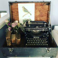 an old fashioned typewriter sitting on top of a table next to flowers and books