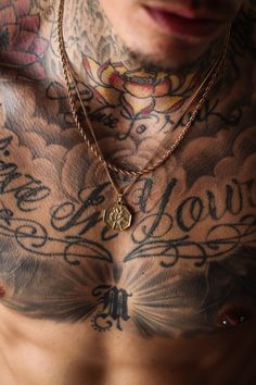 a man with tattoos on his chest wearing a gold chain and a heart charm necklace