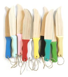 several different colored wooden knives lined up in a row on a white background with string