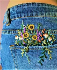 a woman's jeans with flowers embroidered on the side and back pocket, in front of her belly