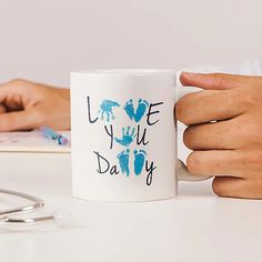 two hands holding a coffee mug with the words i love you daddy on it next to a pair of eyeglasses