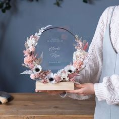 a woman holding a wooden box with flowers on it and a plaque in front of her