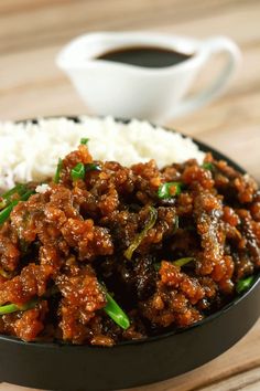 a bowl filled with meat and rice next to a cup of coffee on a table