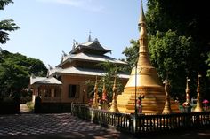 a large golden pagoda sitting in the middle of a park next to a fence and trees