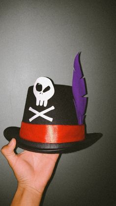 a hand holding a hat with a skull and feather on it