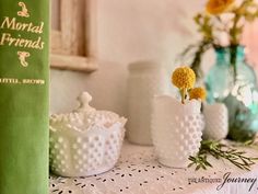 three white vases with yellow flowers in them on a table next to a green book