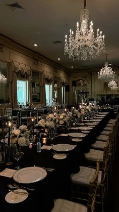 an elegant dining room set up with black table cloths and white dinnerware, chandeliers and centerpieces