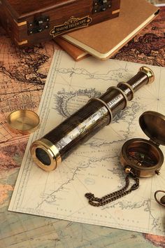 an old brass telescope sitting on top of a map next to other antique pocket watches