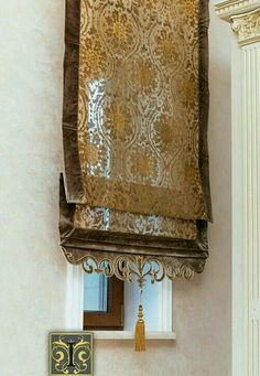 an ornate gold and brown window valance hanging from the side of a white wall