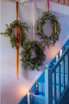 two wreaths are hanging on the wall next to some stairs with candles in them