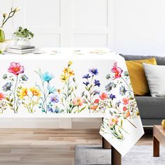 the table cloth is decorated with watercolor flowers on it, and sits in front of a gray couch