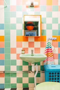 a bathroom with colorful tiles on the walls and a green sink in the middle, next to a blue trash can