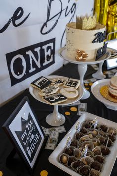 a table topped with cakes and desserts on top of it's tables covered in black and gold confetti