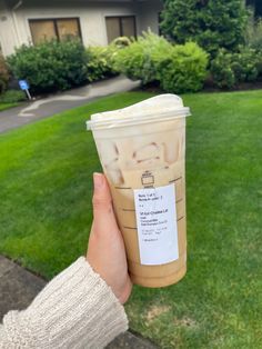 a person holding up a cup of coffee in front of a house on the grass