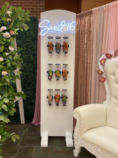 there is a white chair next to a wall with candy cups on it and a sign that says sweet 16