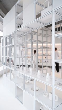 a room filled with lots of white shelves covered in glass containers and people standing around