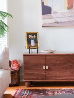 a living room with a large painting on the wall next to a dresser and chair