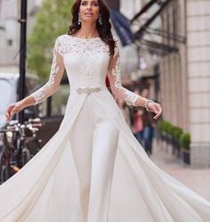 a woman is walking down the street wearing a long white dress with sheer sleeves and lace detailing