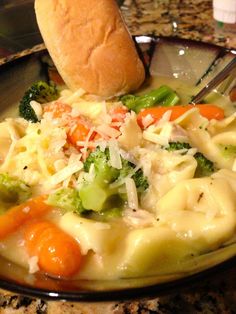 a bowl filled with pasta, carrots and broccoli next to a roll