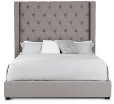 an upholstered bed with white pillows and gray linens on the headboard