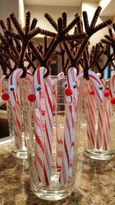 some candy canes and reindeer noses are in glass cups on a counter top with chocolate sticks sticking out of them