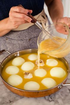 a woman pouring sauce on some food in a pan